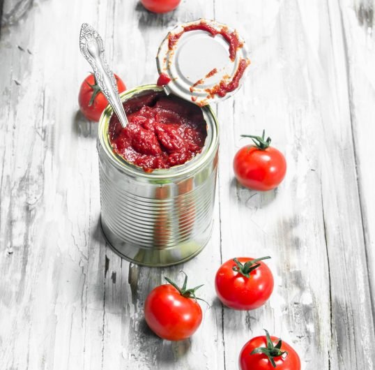 Tomato sauce in a tin can with a spoon and tomatoes.