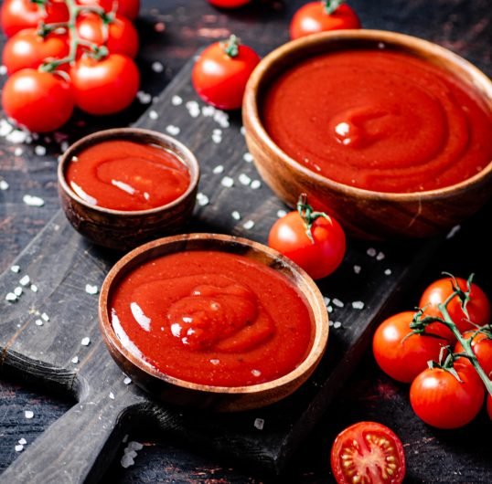 Tomato sauce on a wooden cutting board with pieces of salt.